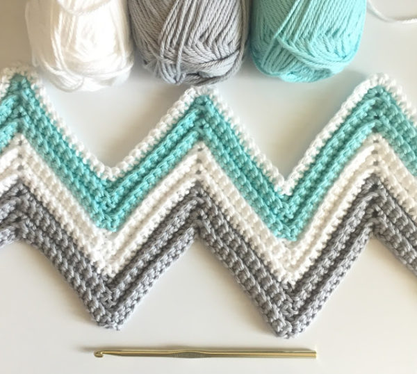 close up of teal gray and white chevon blanket in progress with yarn and hook