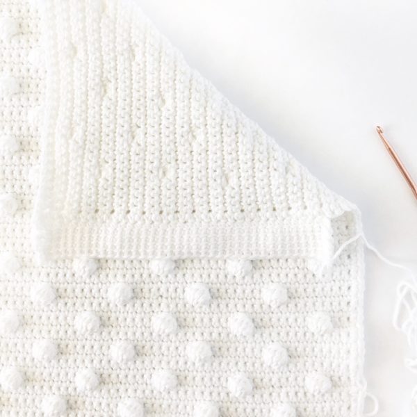 white polka dot crochet blanket laying flat with hook