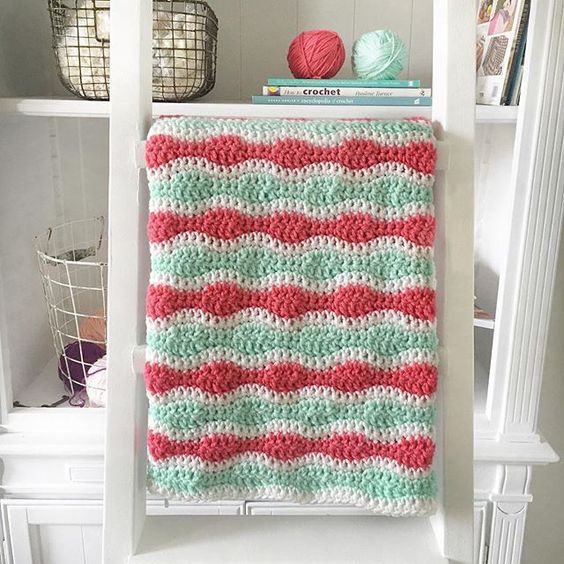 Mint and Coral Single and Double Crochet Blanket hanging on white ladder in front of bookcase