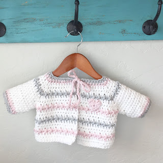 Crochet Baby Sweater in White, Pink and Gray hanging on a hook