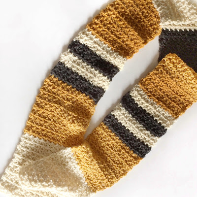 flat lay of crochet modified moss stitch scarf in gold black and cream