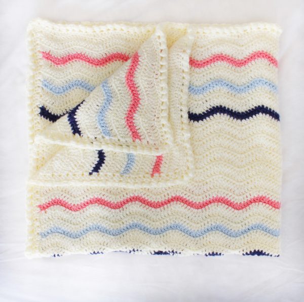folded blanket laying flat of crochet ripple stitch with cream yarn and blue and pink stripes