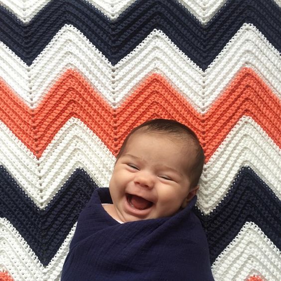 smiling baby laying white navy and orange crochet chevron blanket