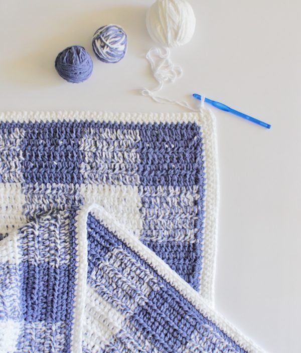 crochet blue and white gingham blanket laying flat with yarn