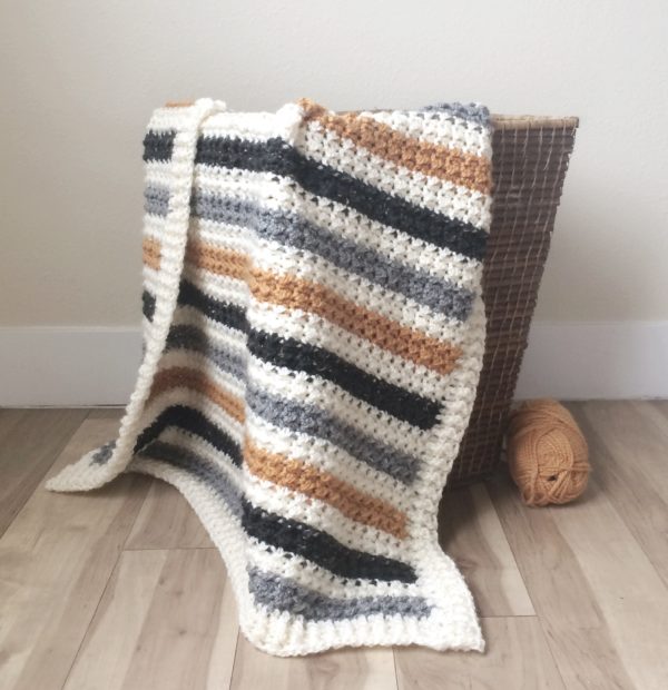 white black and gold crochet striped even moss stitch blanket draped over basket