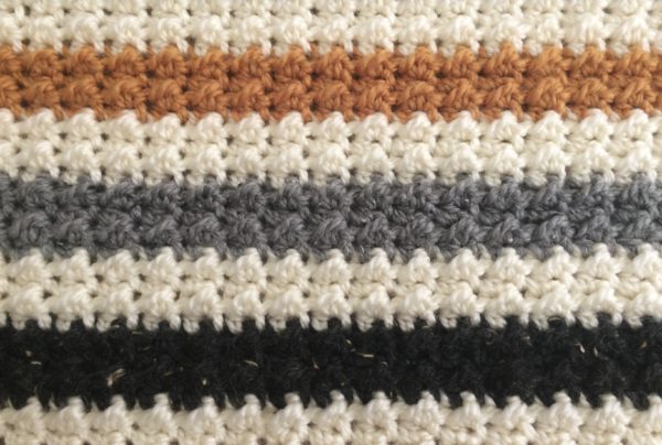 close up crochet striped even moss stitch blanket in white black and gold