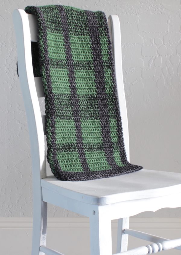 crochet black and green plaid blanket draped over white chair