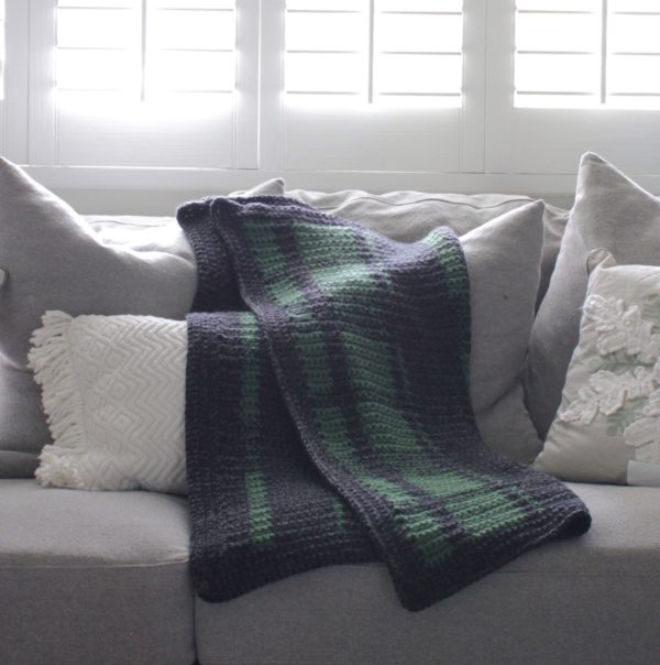 crochet black and green plaid blanket laying on gray couch
