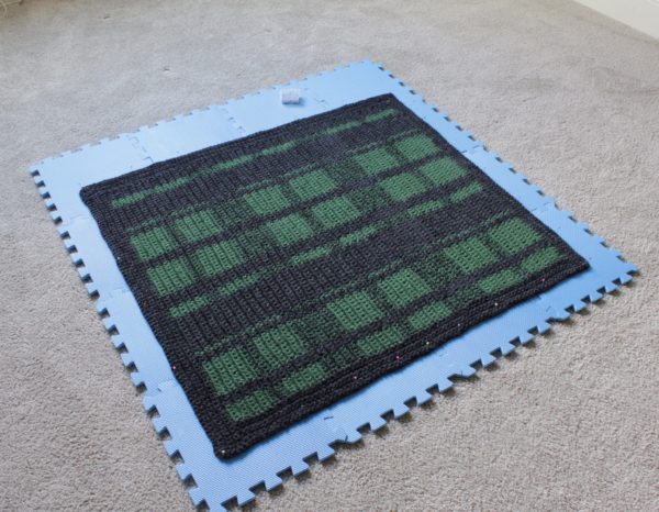 crochet green and black plaid blanket laying flat on foam boards