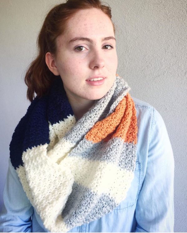 red haired girl wearing white gray navy and orange crochet infinity scarf