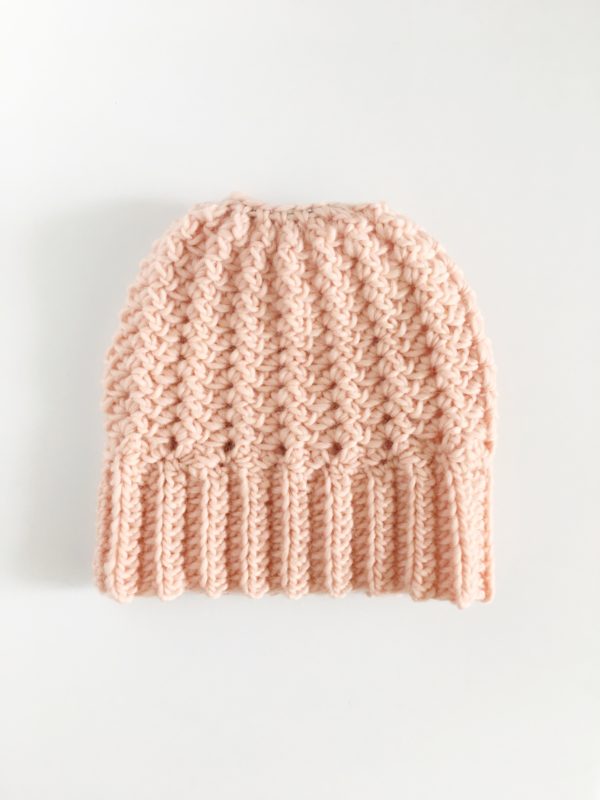 peach color crochet sprig stitch bun beanie laying flat on white background