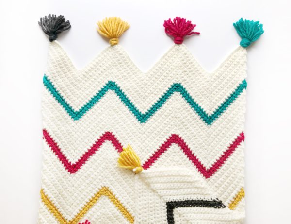cream blanket with teal black gold and red chevron stripes with tassels laying flat on white background