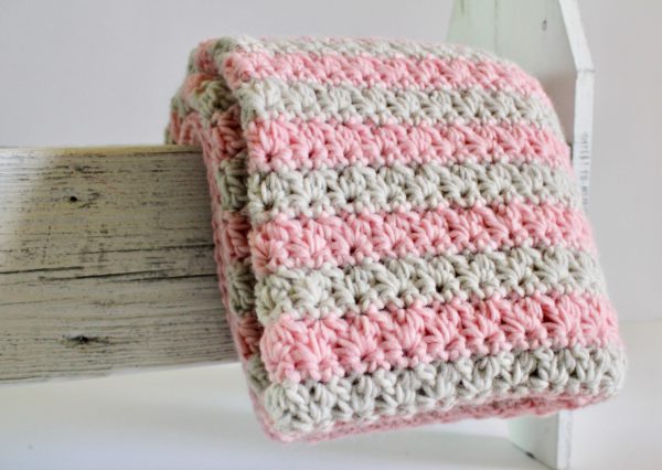 Crochet Mixed Cluster Stitch Blanket with Pink and Gray yarn draped over the side of wooden box