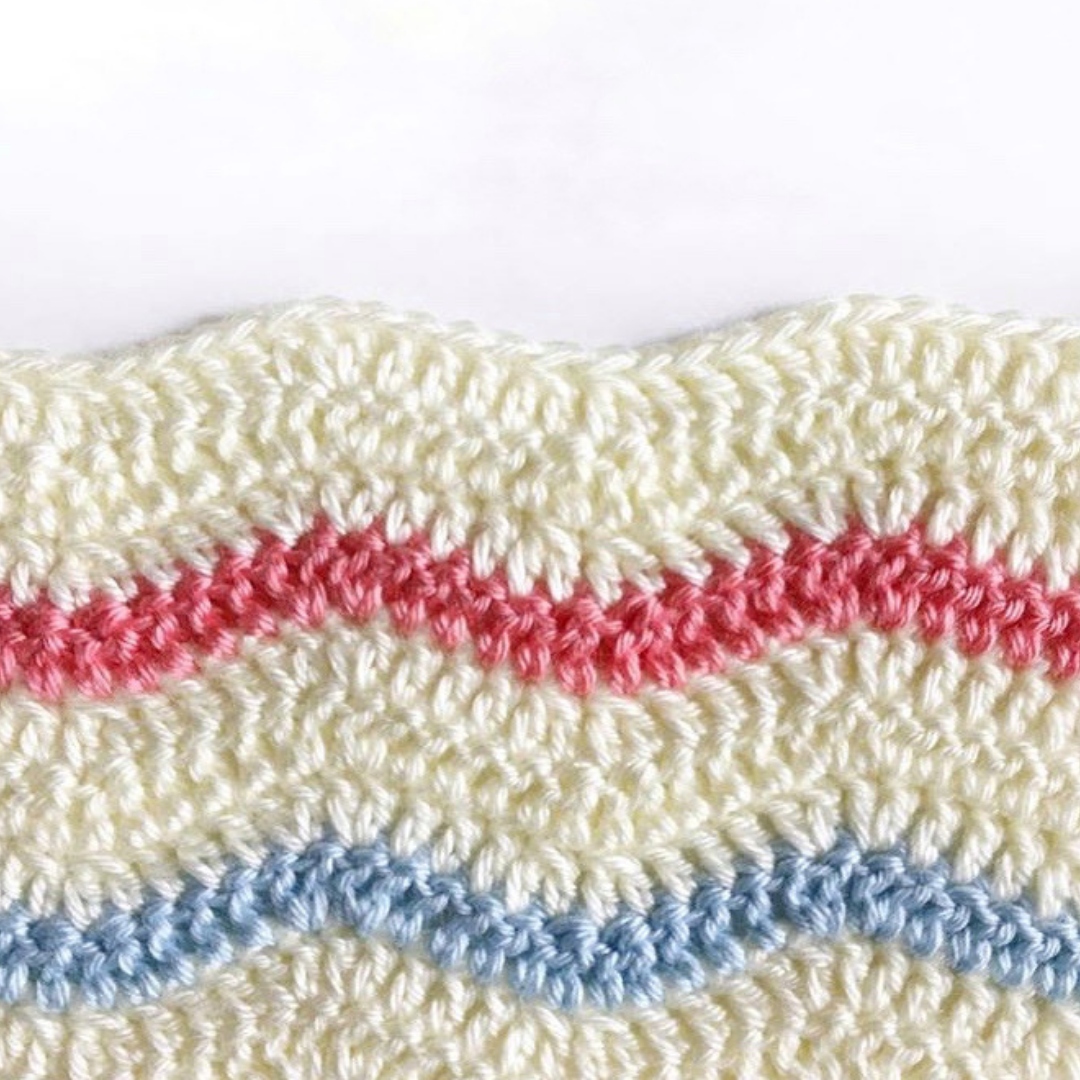 close up of crochet ripple stitch with cream yarn and blue and pink stripes