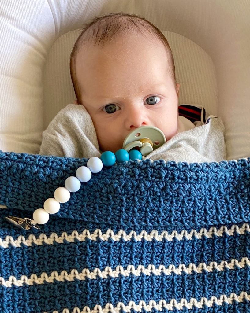baby with blue crochet blanket with thin white stripes
