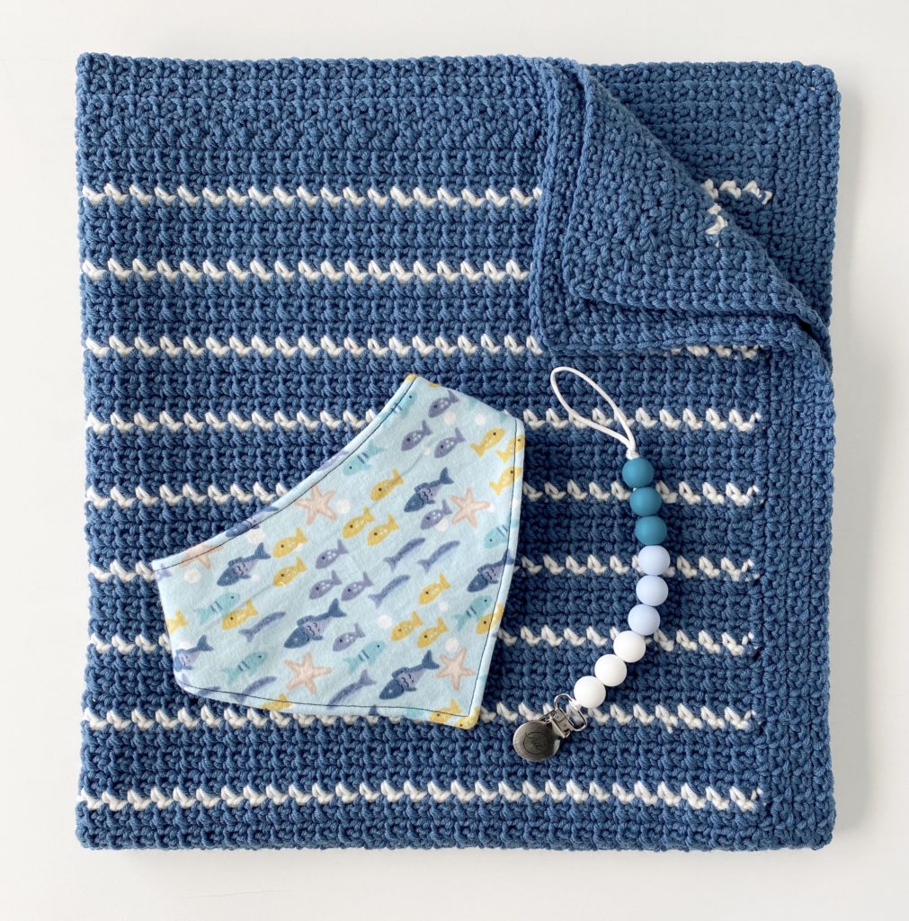 blue crochet blanket with thin white stripes with baby bib and pacifier clip