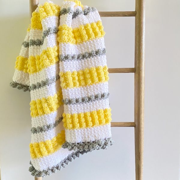 textured gray yellow white baby blanket on ladder