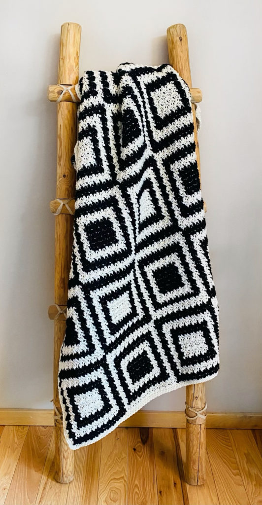 black and white squares crochet blanket hanging on ladder
