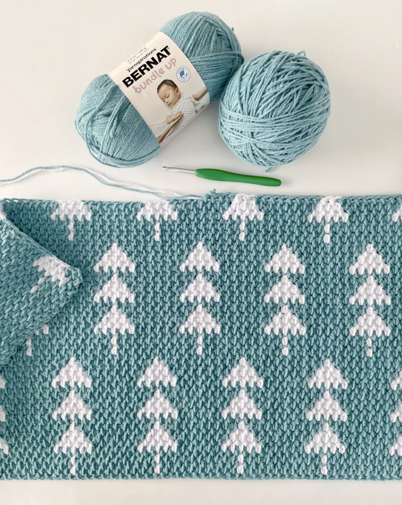 flat lay of crochet teal blanket in progress with white trees with yarn and hook