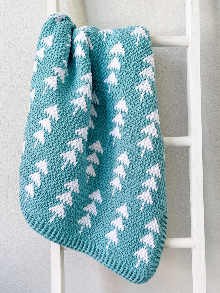 crochet teal blanket with white trees hanging on white ladder
