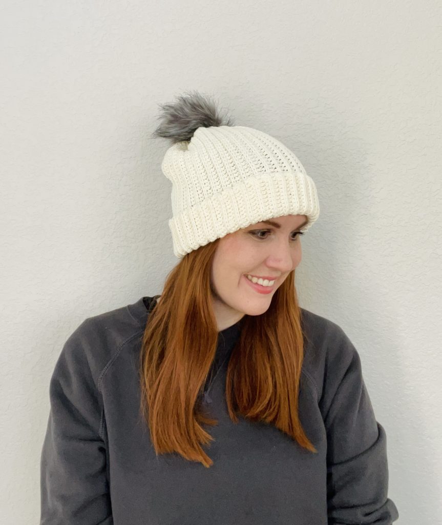 red haired woman wearing cream cotton crochet pom pom beanie