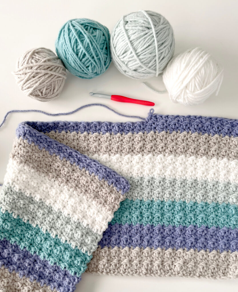 crochet blanket with gray and blue stripes with balls of yarn