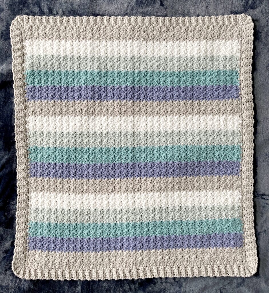 crochet blanket with gray and blue stripes laying flat