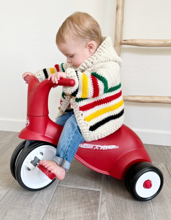 baby wearing crochet sweater on ride tricycle