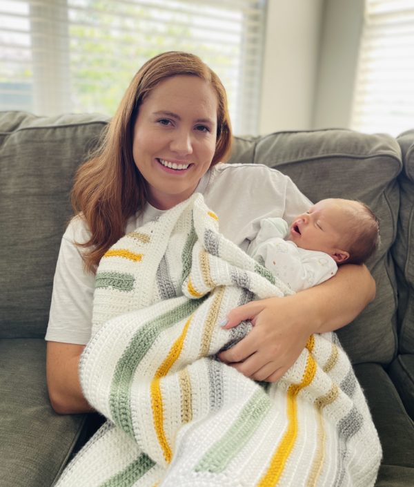 girl holding newborn in a striped crochet blanket