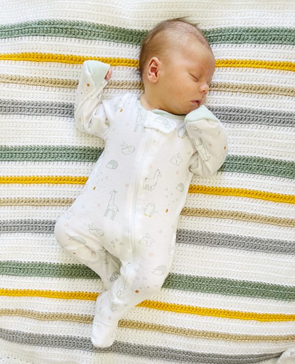 newborn laying on a striped crochet blanket. Colors are light gold and sage and white