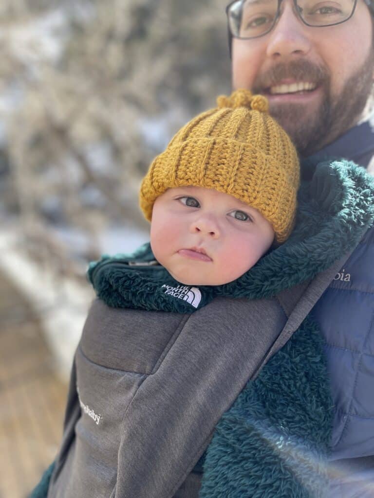 Father carrying baby son wearing yellow crochet hat