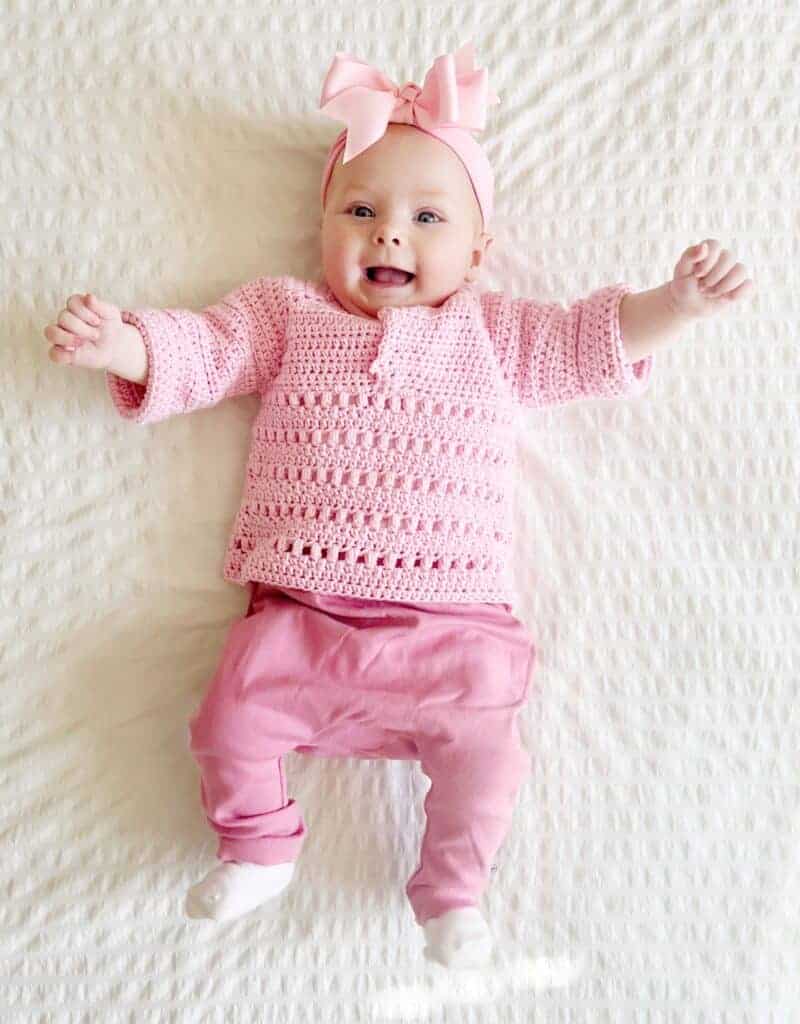 baby girl smiling wearing a pink crochet baby sweater. 