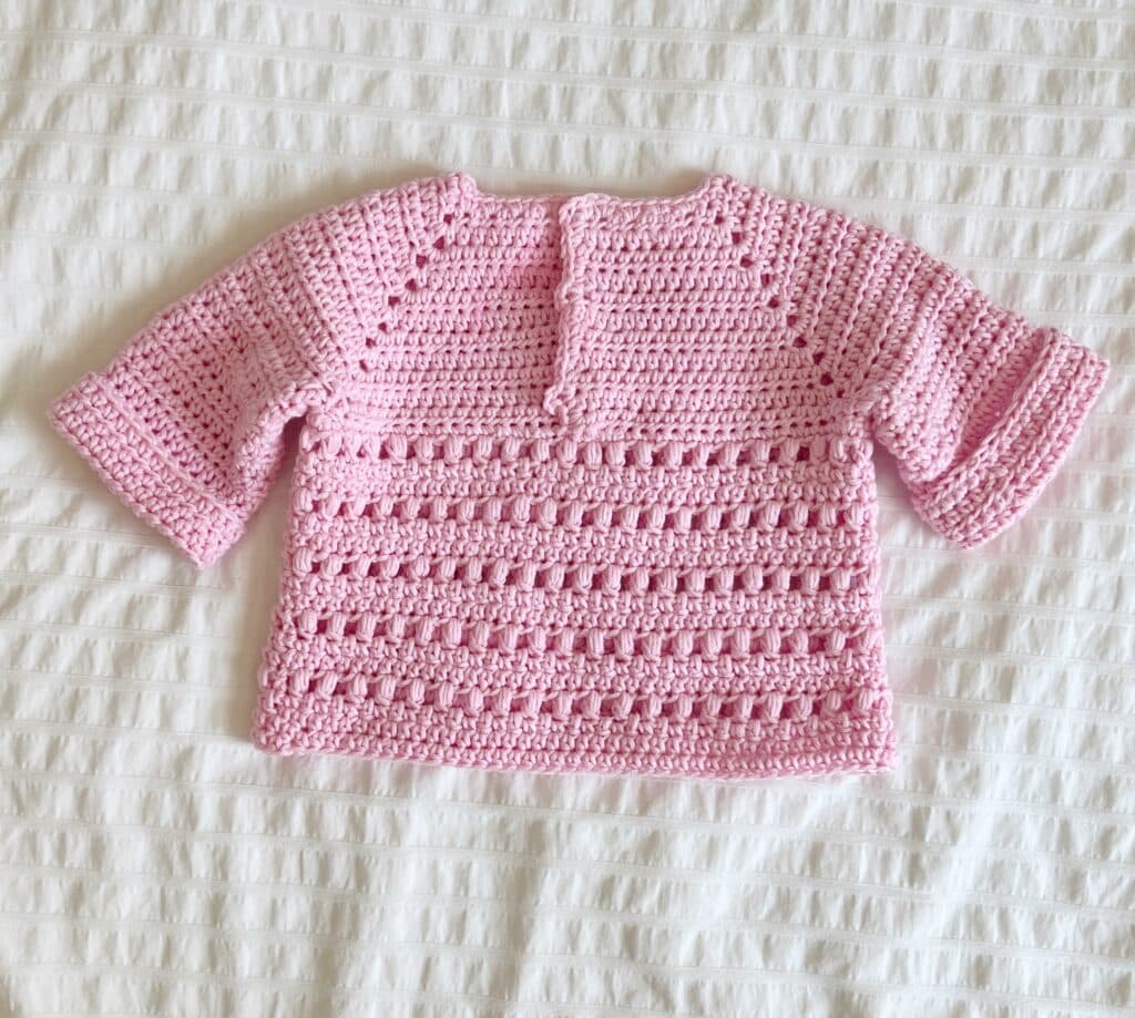crochet pink sweater laying flat with with white background