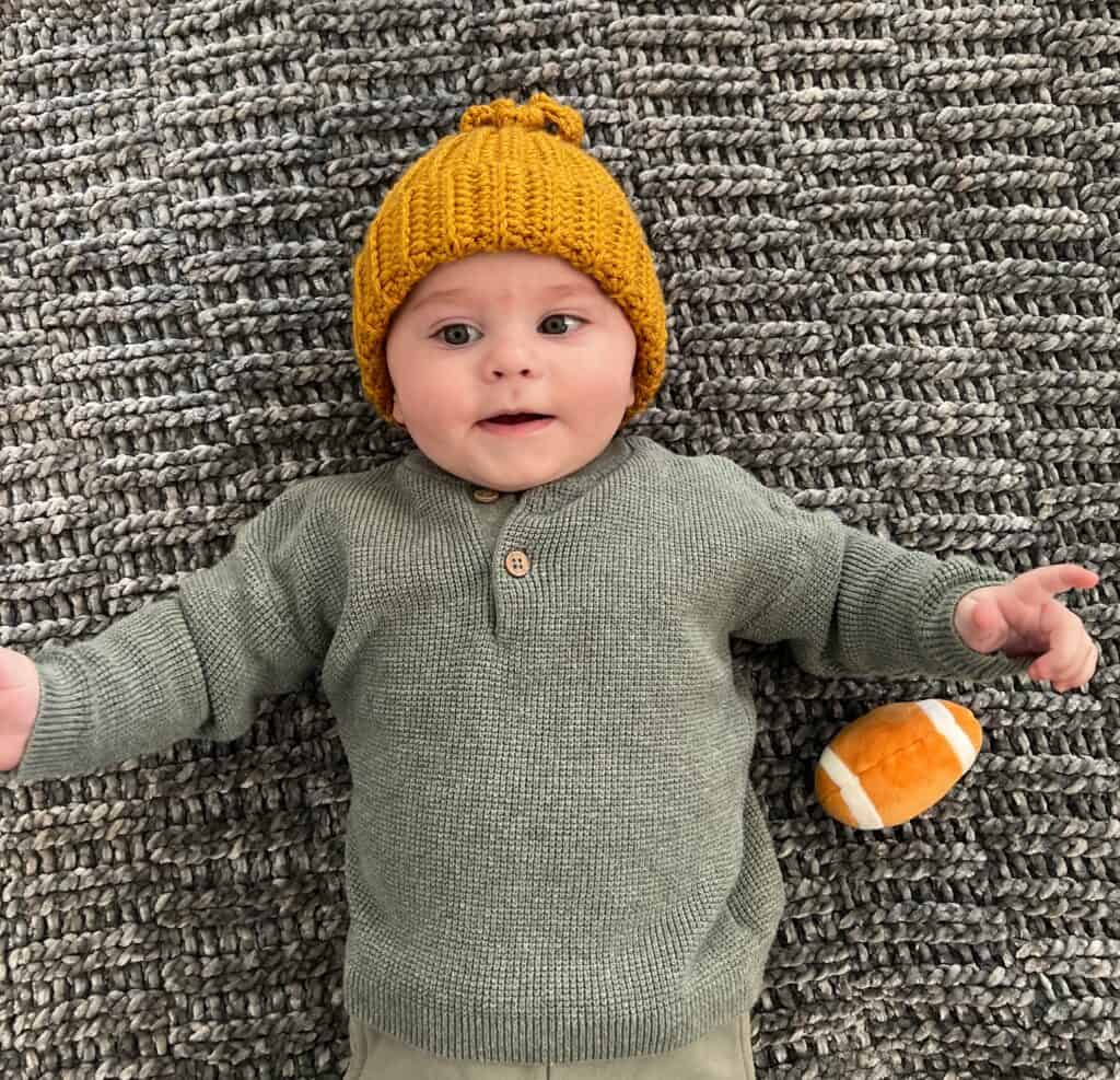 little baby wearing yellow crochet hat on crochet play mat