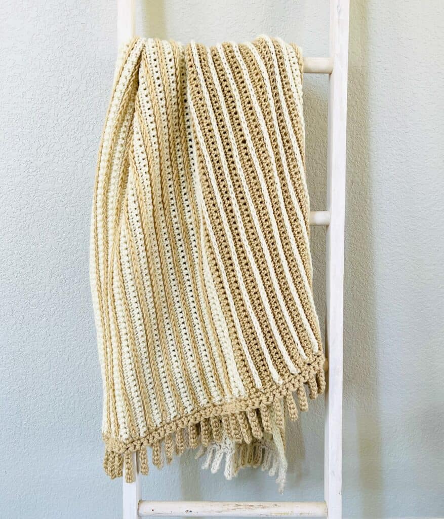 yellow and white crochet blanket hanging on the ladder 