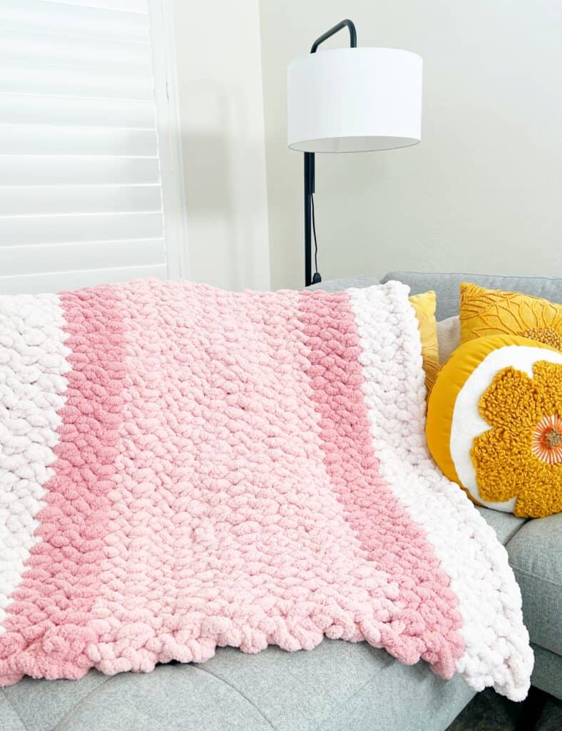 pink and white crochet blanket on gray couch
