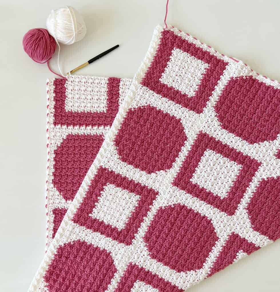 pink and white crochet blanket with yarn skeins and crochet hook