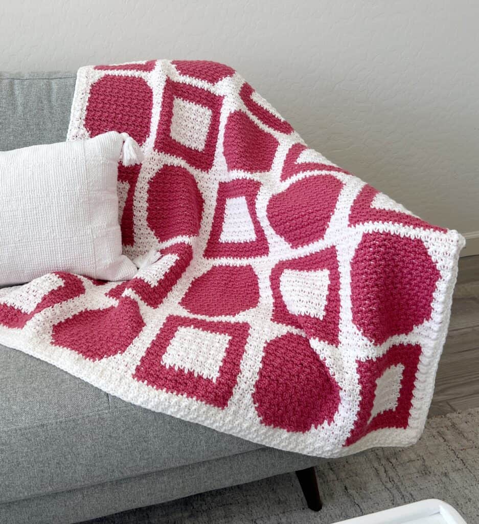 pink and white crochet blanket hanging over couch