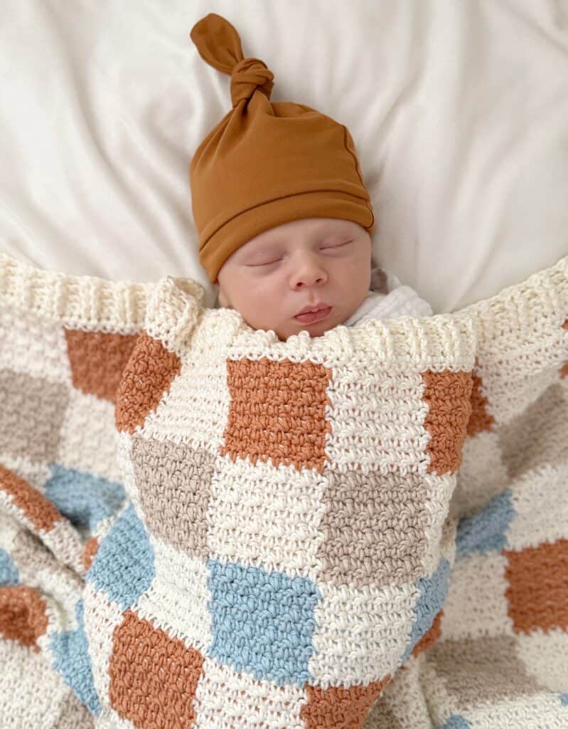 Baby Boy snuggled under checkered crochet blanket