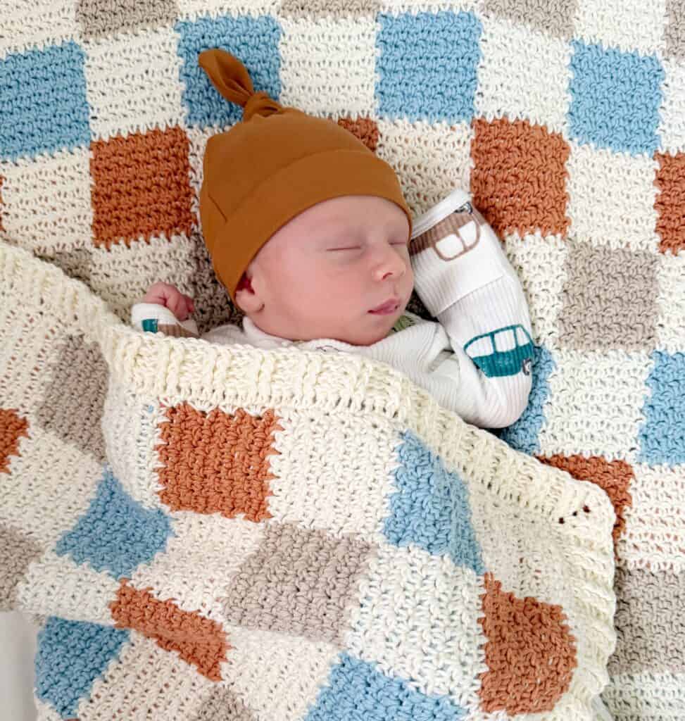 Baby boy snuggled under crochet checkerboard blanket