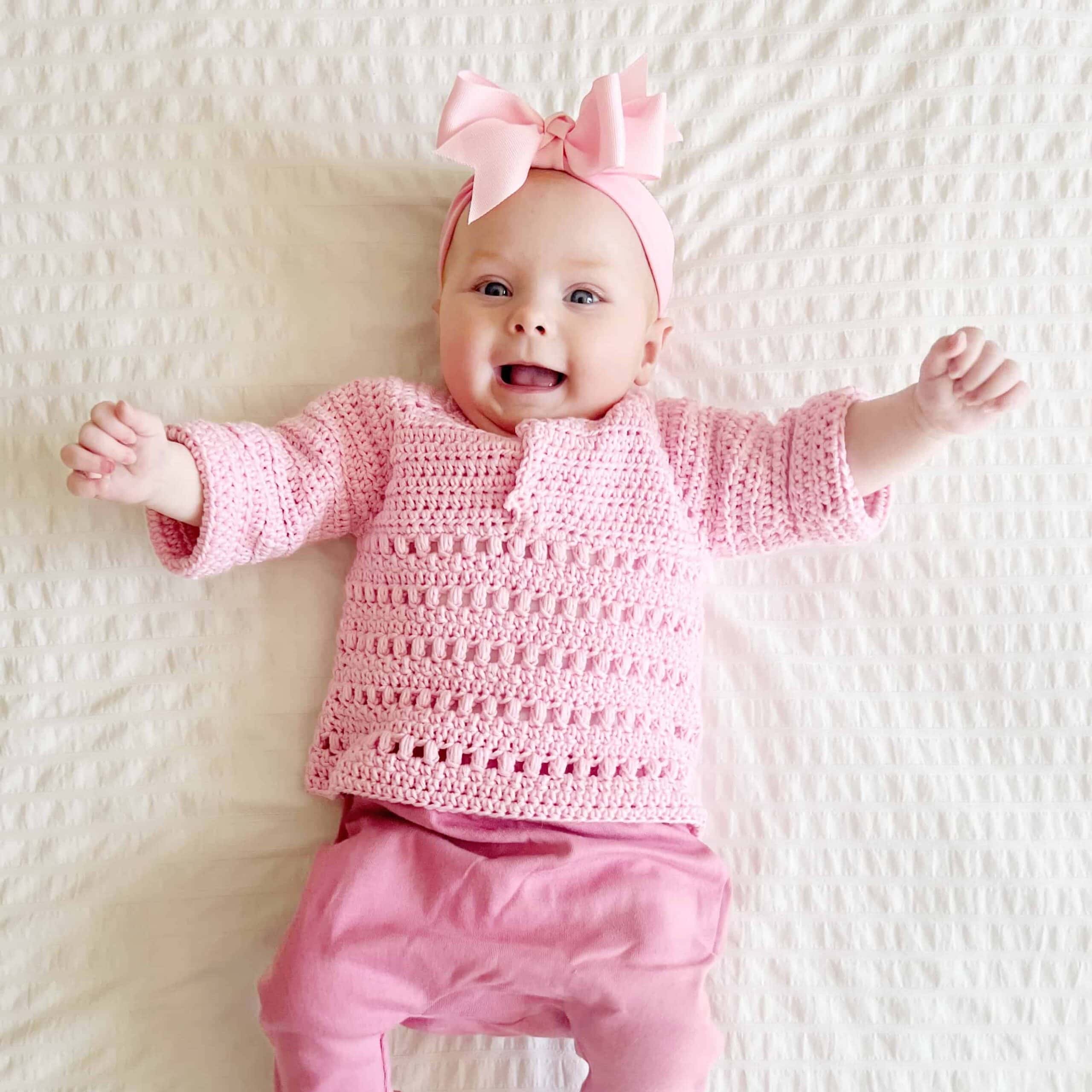 baby girl smiling wearing a pink crochet baby sweater.