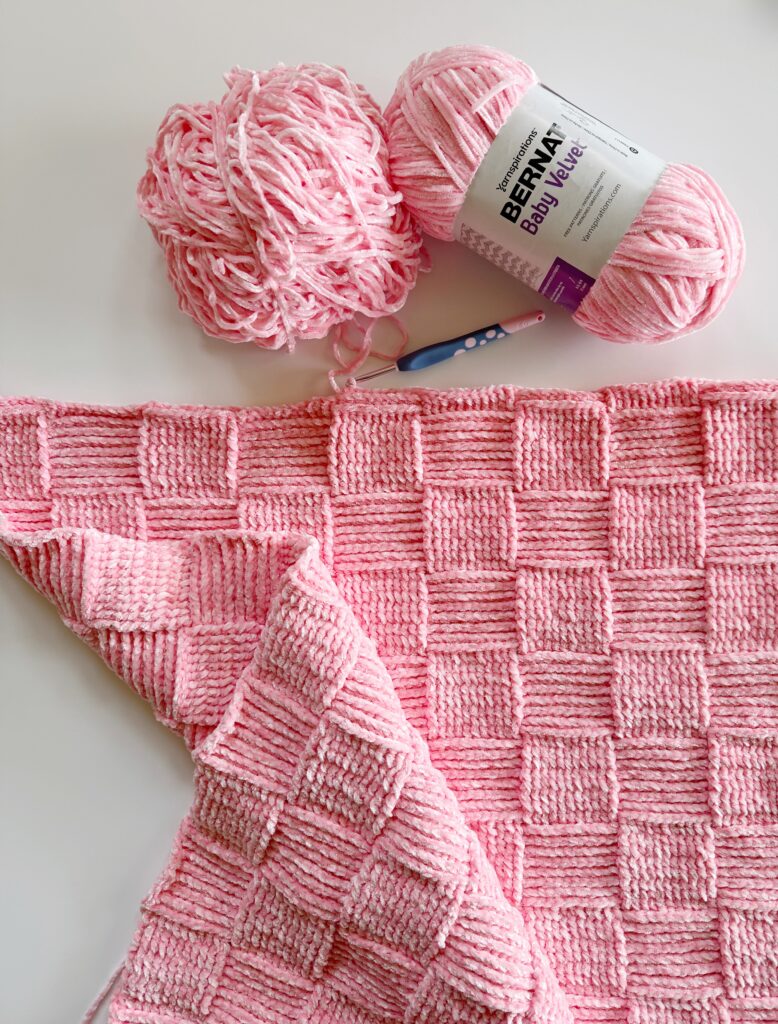 flat lay of pink basketweave blanket with Bernat baby velvet skein and crochet hook
