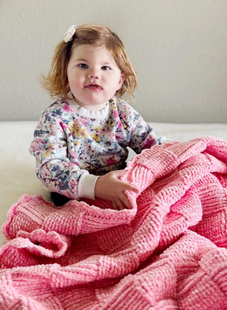 baby girl snuggled under pink crochet basketweave blanket